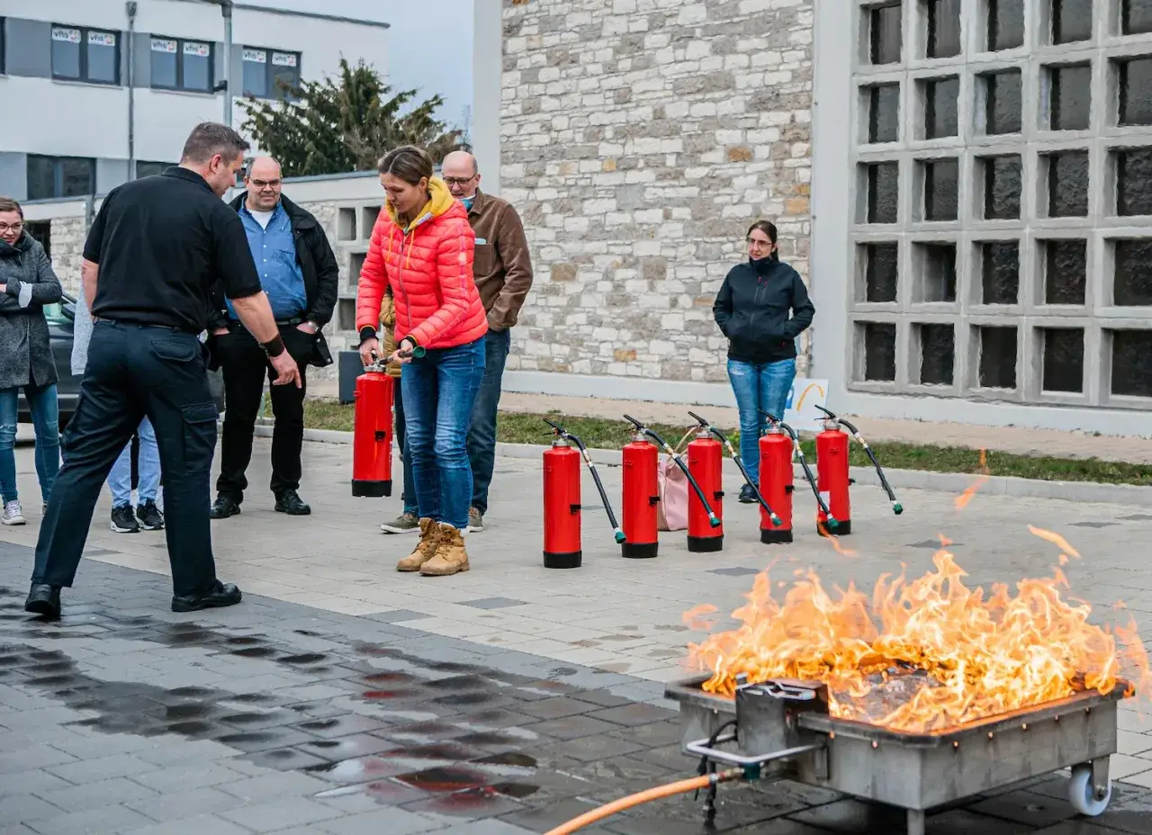 Teilnehmer einer Fortbildung Brandschutzhelfer &uuml;ben den Umgang mit Feuerl&ouml;schern an einer Feuerschale.