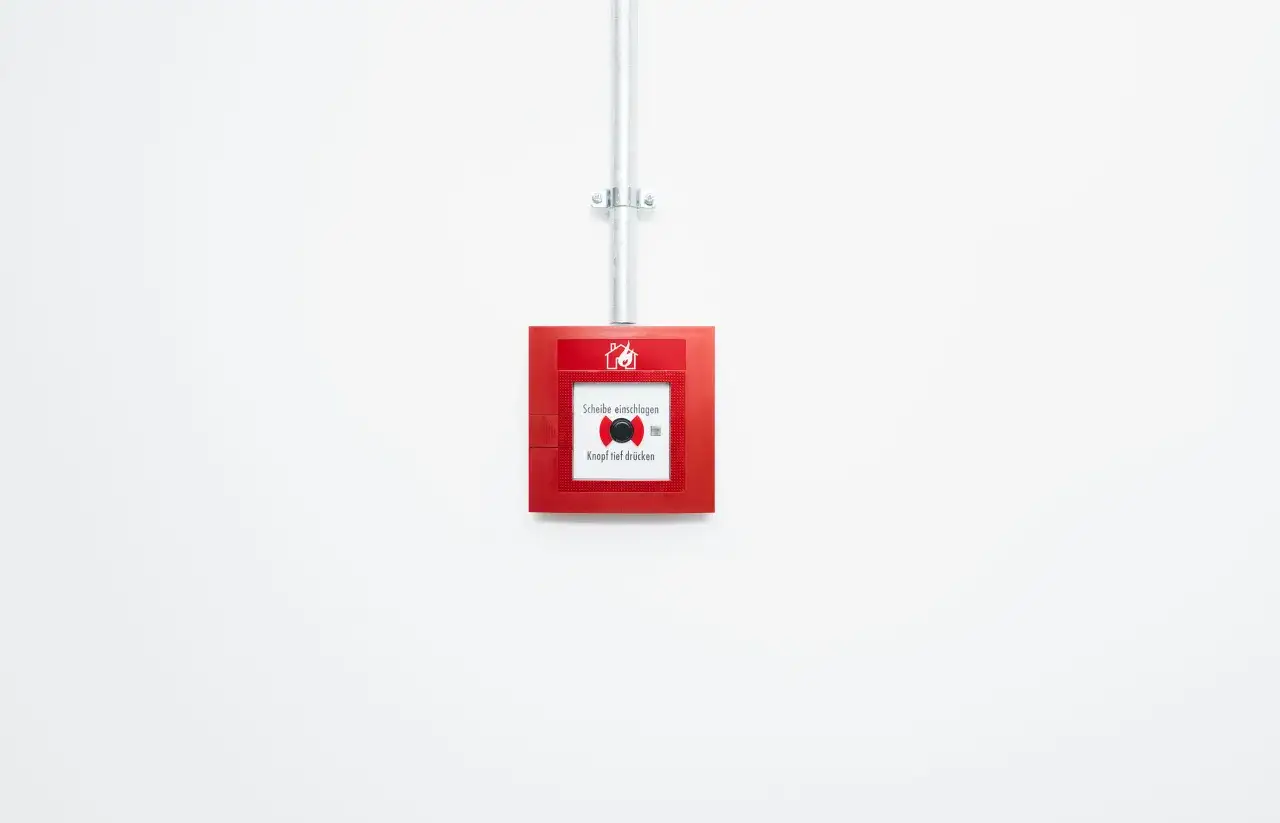 Roter Feuermelder an weißer Wand, wie in der Landesbauordnung Bremen vorgeschrieben.