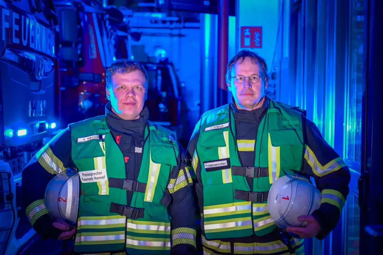 Zwei M&auml;nner in Feuerwehruniformen, beide mit der Aufschrift 