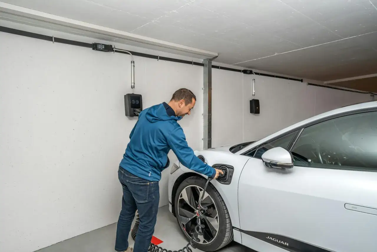 Mann l&auml;dt E-Auto in Tiefgarage. Wallbox mit Brandschutz-Vorrichtung.