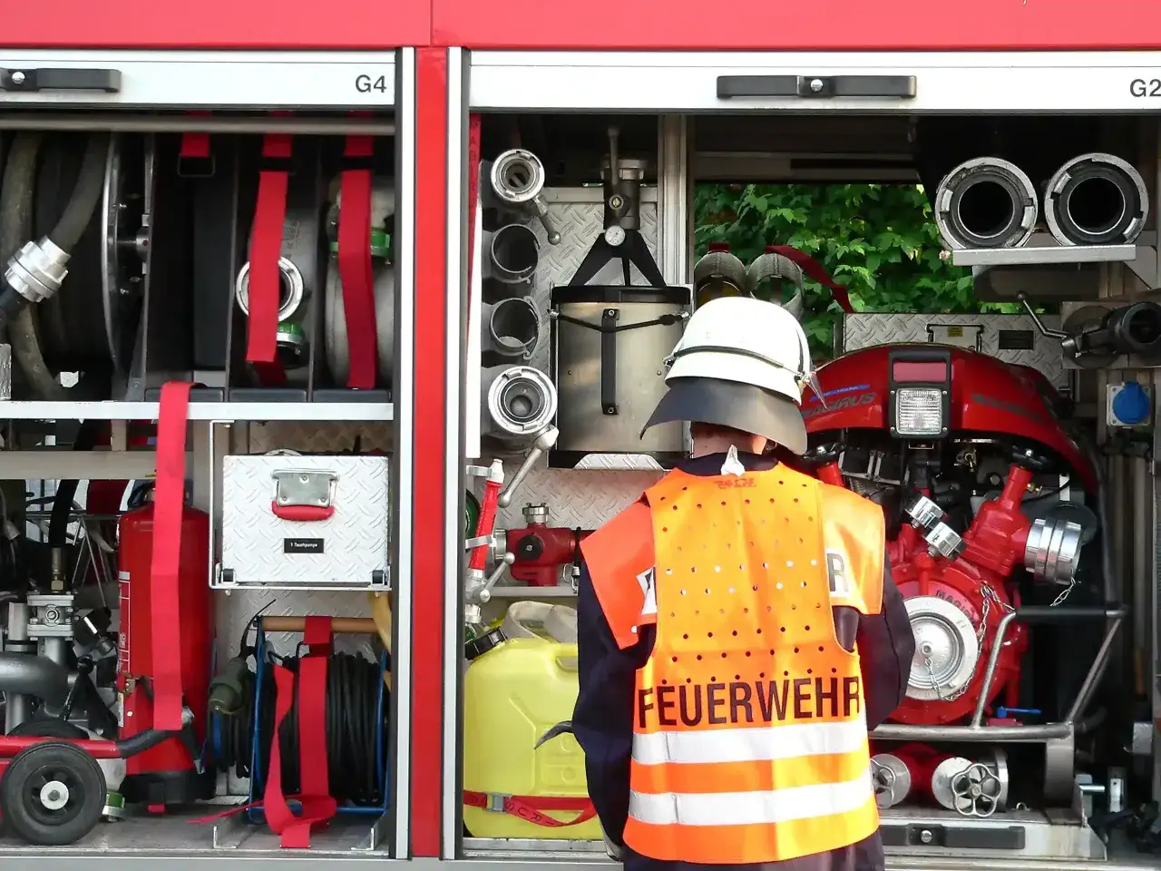 Feuerwehrmann in Warnweste vor einem L&ouml;schfahrzeug mit Schl&auml;uchen und Pumpe. Die Ausr&uuml;stung zeigt die berufsfeuerwehr voraussetzungen f&uuml;r den Einsatz.