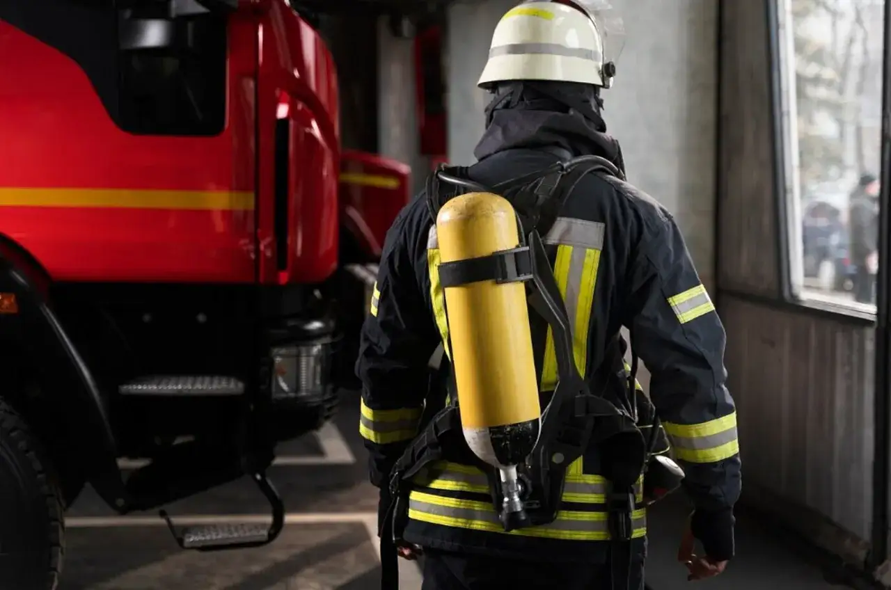 Feuerwehrmann in voller Montur mit Atemschutzgerät, bereit für den Einsatz. Ein Mitglied der ehrenamtlichen Feuerwehr, neben einem roten Feuerwehrauto.