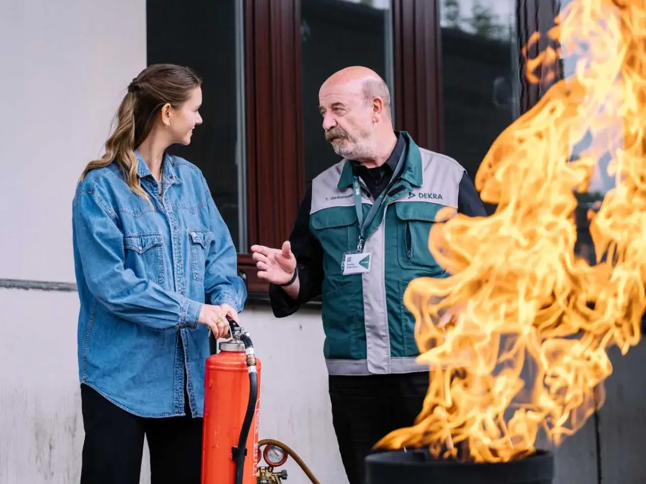 Ein DEKRA-Mitarbeiter erklärt einer Frau mit Feuerlöscher, wer Sicherheitsbeauftragte ausbilden darf.