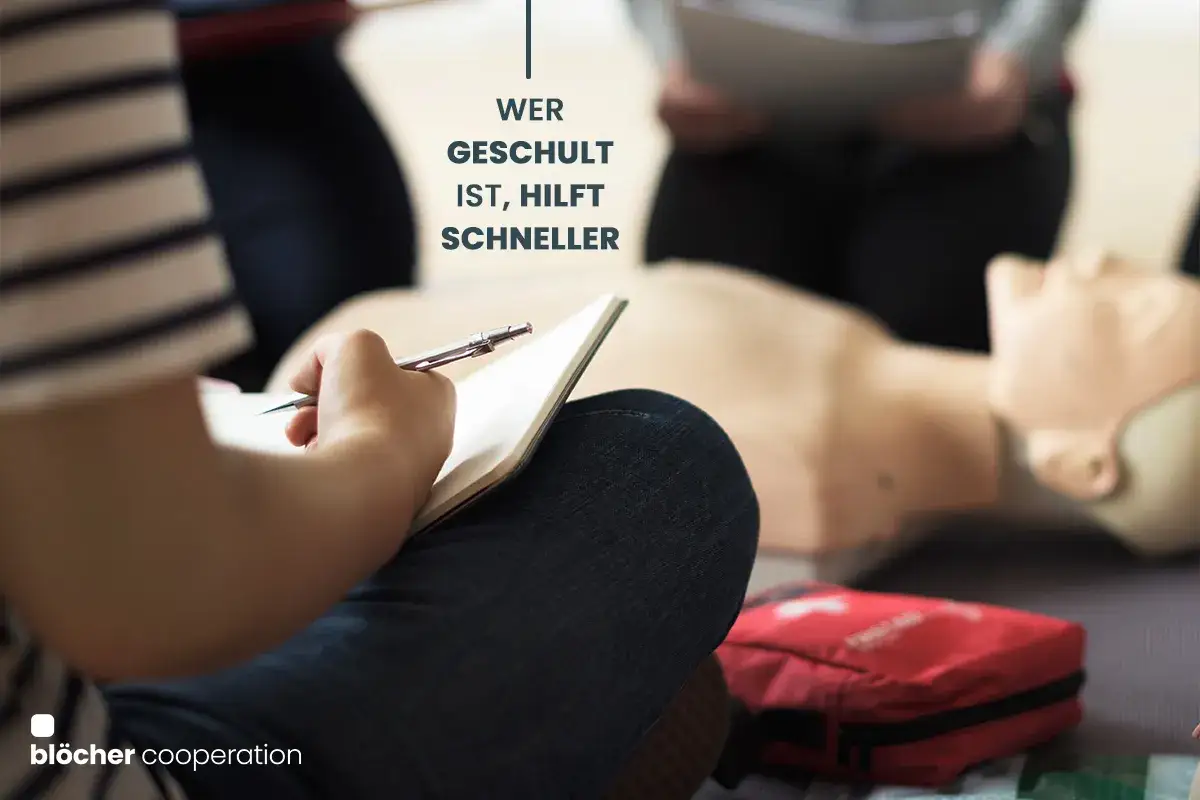 Person macht Notizen w&auml;hrend einer unterweisung erste hilfe. Ein &Uuml;bungspuppe und ein Erste-Hilfe-Kasten sind im Hintergrund zu sehen.