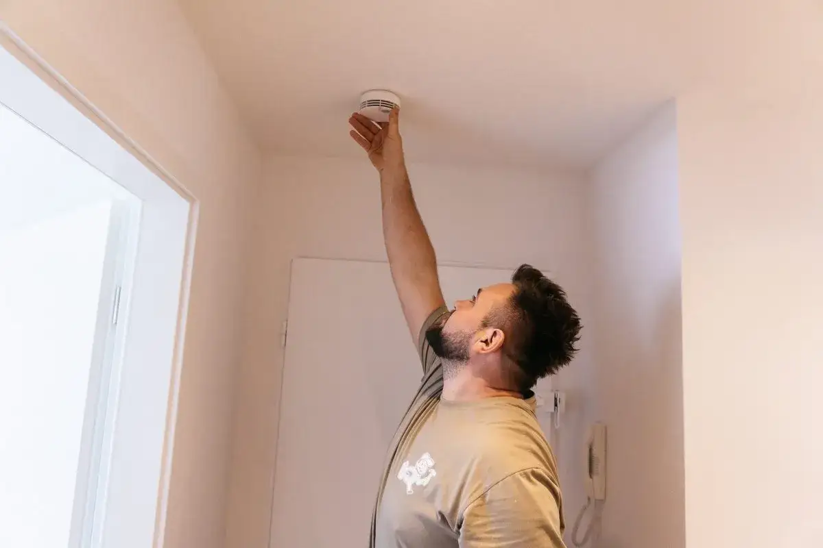 Mann montiert Rauchmelder an der Decke. Rauchmelderpflicht in Bayern beachten!
