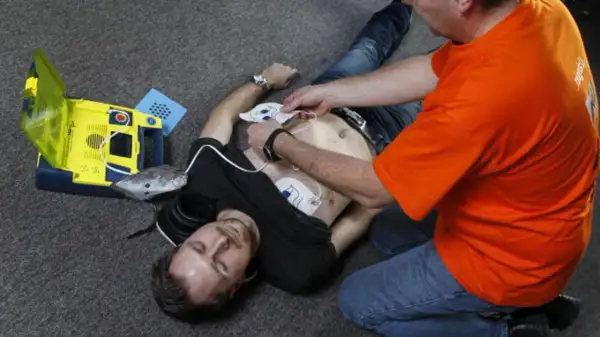 Mann legt Elektroden eines Defibrillators an, um Leben zu retten. Wann Defibrillator? Jetzt!