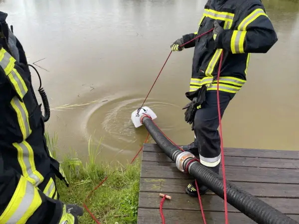Feuerwehrleute führen eine wasserentnahme offenes gewässer fwdv 3 durch. Ein Tauchpumpen-Ansaugschlauch wird ins trübe Wasser gelassen.