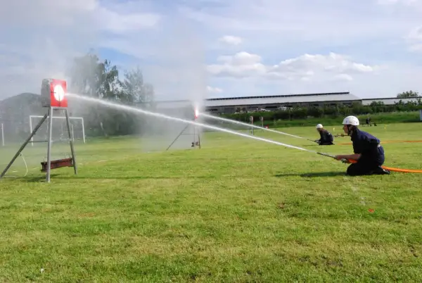 Feuerwehrleute üben einen löschangriff nass aufbau. Sie zielen mit Wasserschläuchen auf Ziele auf einem Feld.