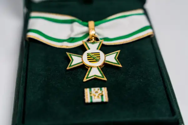 Ein goldenes Kreuz mit weißer und grüner Emaille, das ein Wappen mit schwarzen und gelben Streifen zeigt. Dieses Feuerwehr Ehrenzeichen liegt in einer grünen Samtschachtel.